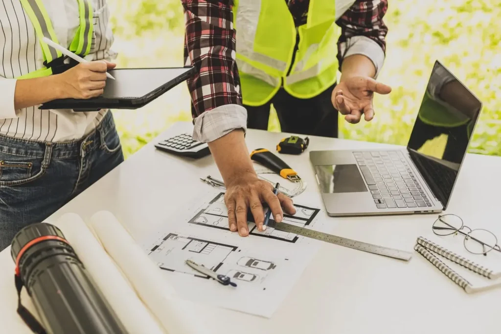 Engineering team reviewing technical blueprints with a laptop and digital tablet to ensure strict quality control for Epic Construction Management.